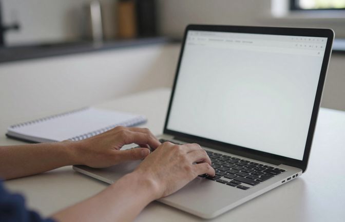 Hands typing on a laptop at a kitchen table