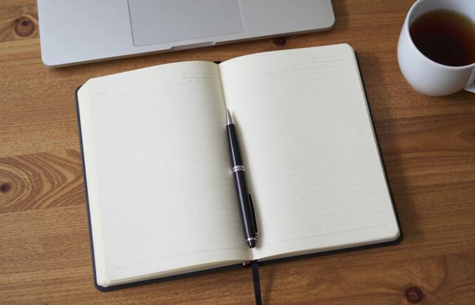 An open paper planner and a printed one-page blank grid on a timber desk with a pen