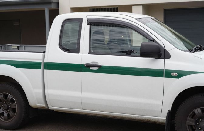 A white dual cab ute parked in a suburban driveway with a plain blank dark green stripe along its doors and no lettering